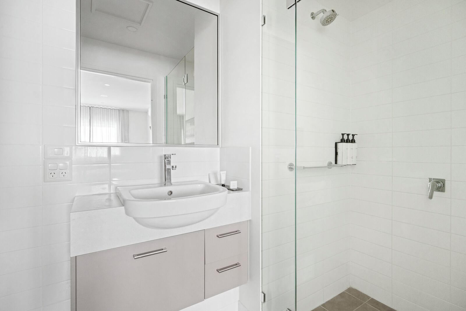 Une salle de bain moderne avec un lavabo blanc, un miroir et une cabine de douche en verre.