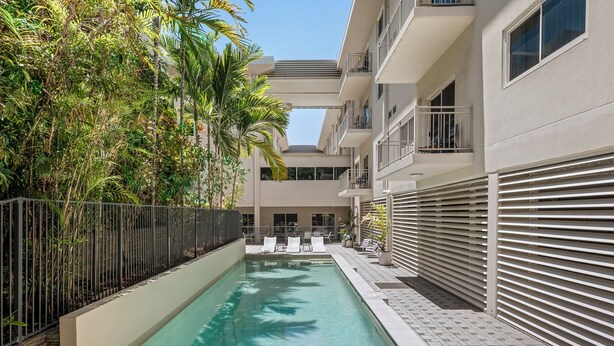 Une piscine entourée d’une clôture et de verdure, avec des chaises longues à proximité.
