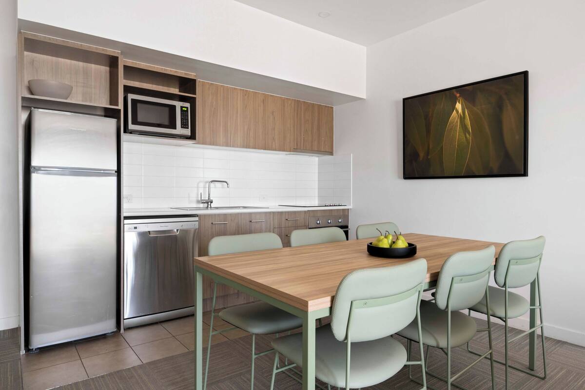 Eine moderne Küche mit Holztisch und Stühlen, inklusive Kühlschrank, Mikrowelle und Geschirrspüler.