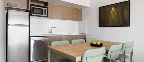 A modern kitchen with a wooden table and chairs, a refrigerator, microwave, and dishwasher.
