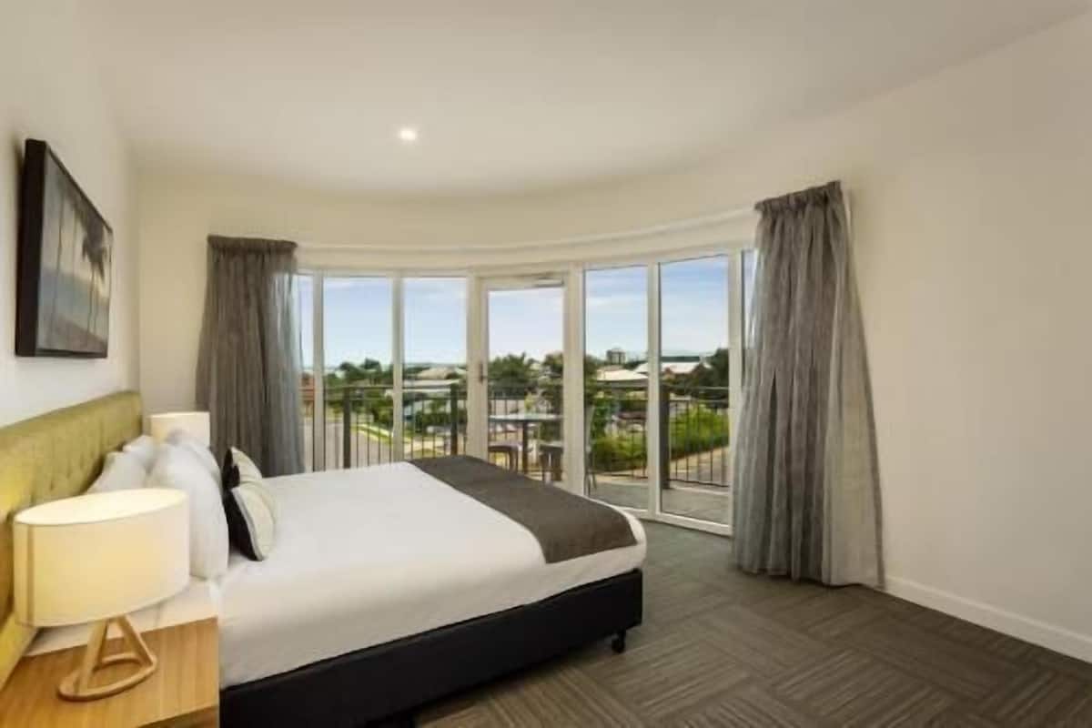 Ein Hotelzimmer mit Bett, Nachttisch, Lampe und Blick ins Freie.