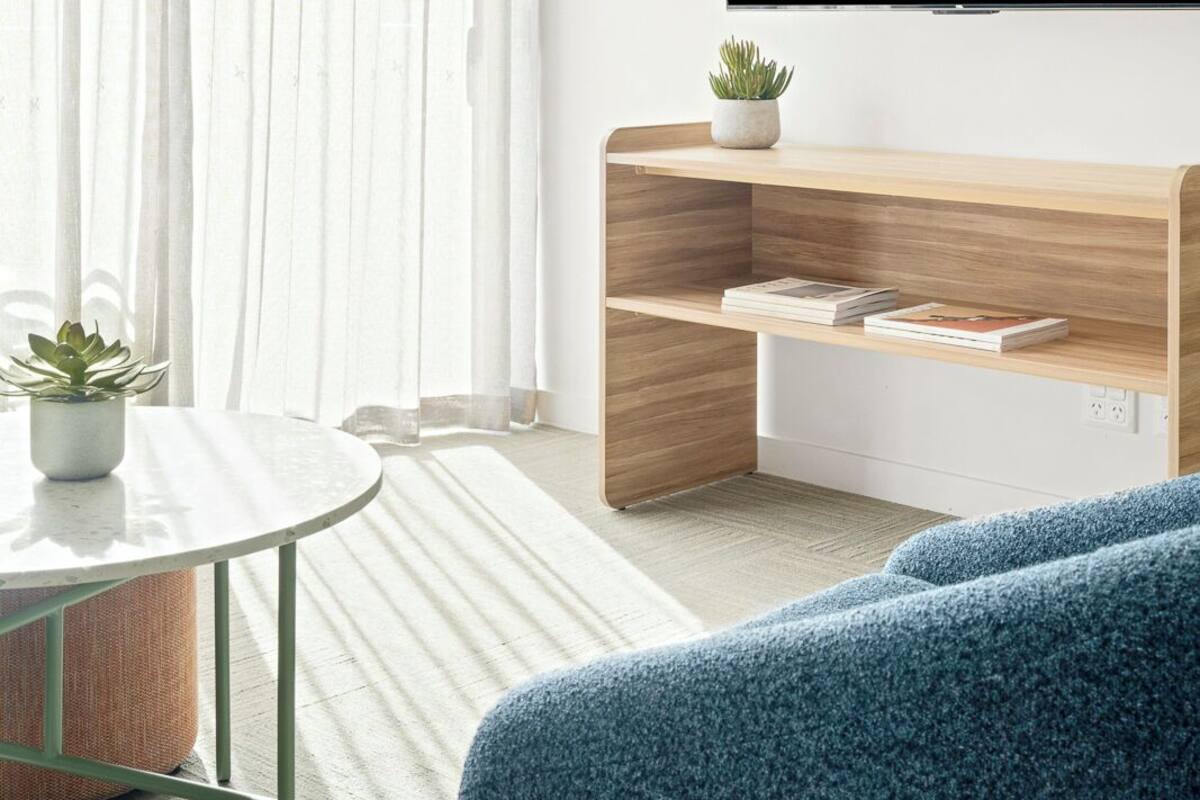 Ein modernes Wohnzimmer mit Wandfernseher, einem Holztischchen, einem runden Couchtisch und einem blauen Sofa.