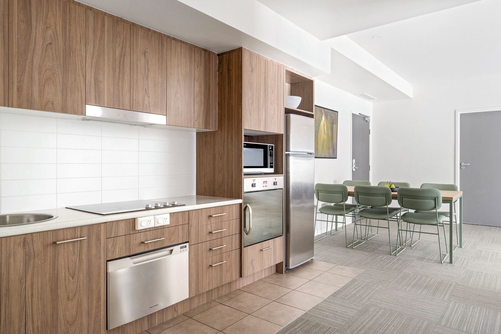 Una cocina moderna con armarios de madera, electrodomésticos de acero inoxidable y un comedor con sillas verdes.