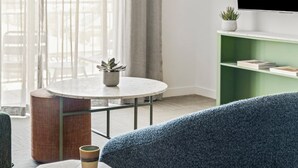 Un salon moderne avec une table ronde, un canapé bleu et un téléviseur posé sur une étagère verte.
