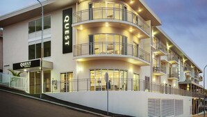 Un hôtel moderne, reconnaissable à son grand panneau « QUEST », doté de nombreux balcons et d’une façade bien éclairée.
