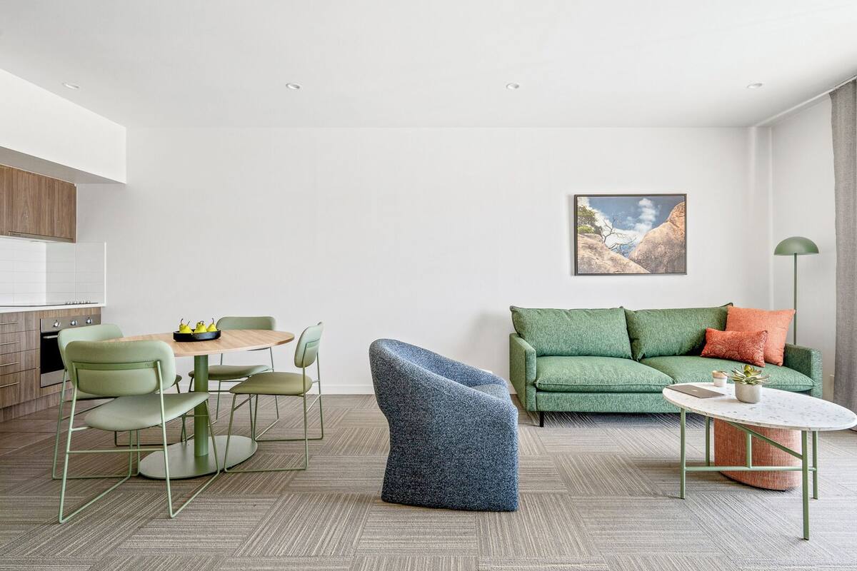 Ein modernes Wohnzimmer mit einem grünen Sofa, einem blauen Sessel und einem Essbereich mit einem Holztisch und grünen Stühlen.