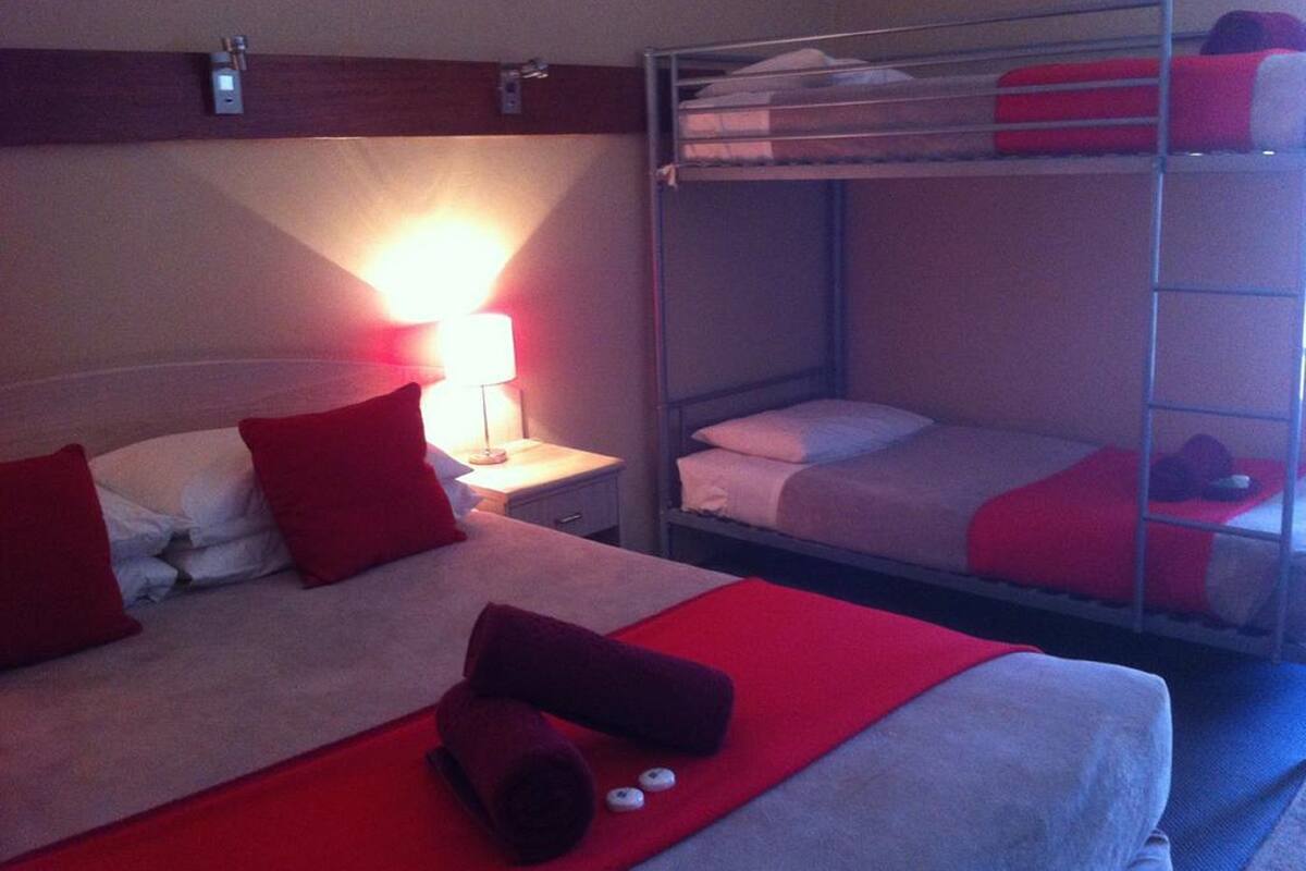 A hotel room with a bunk bed, a single bed, and a nightstand with a lamp.