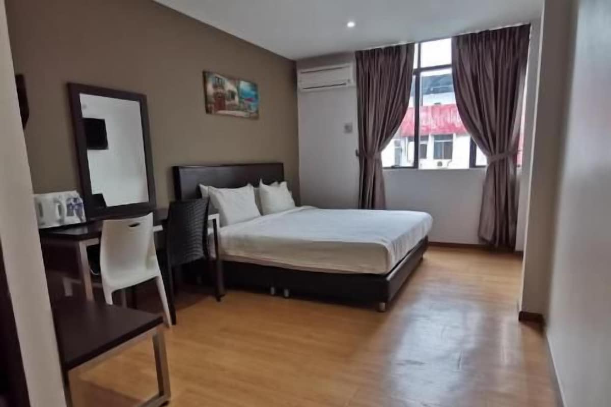 Habitación de hotel con cama, escritorio, silla, un cuadro en la pared y ventana con cortinas.