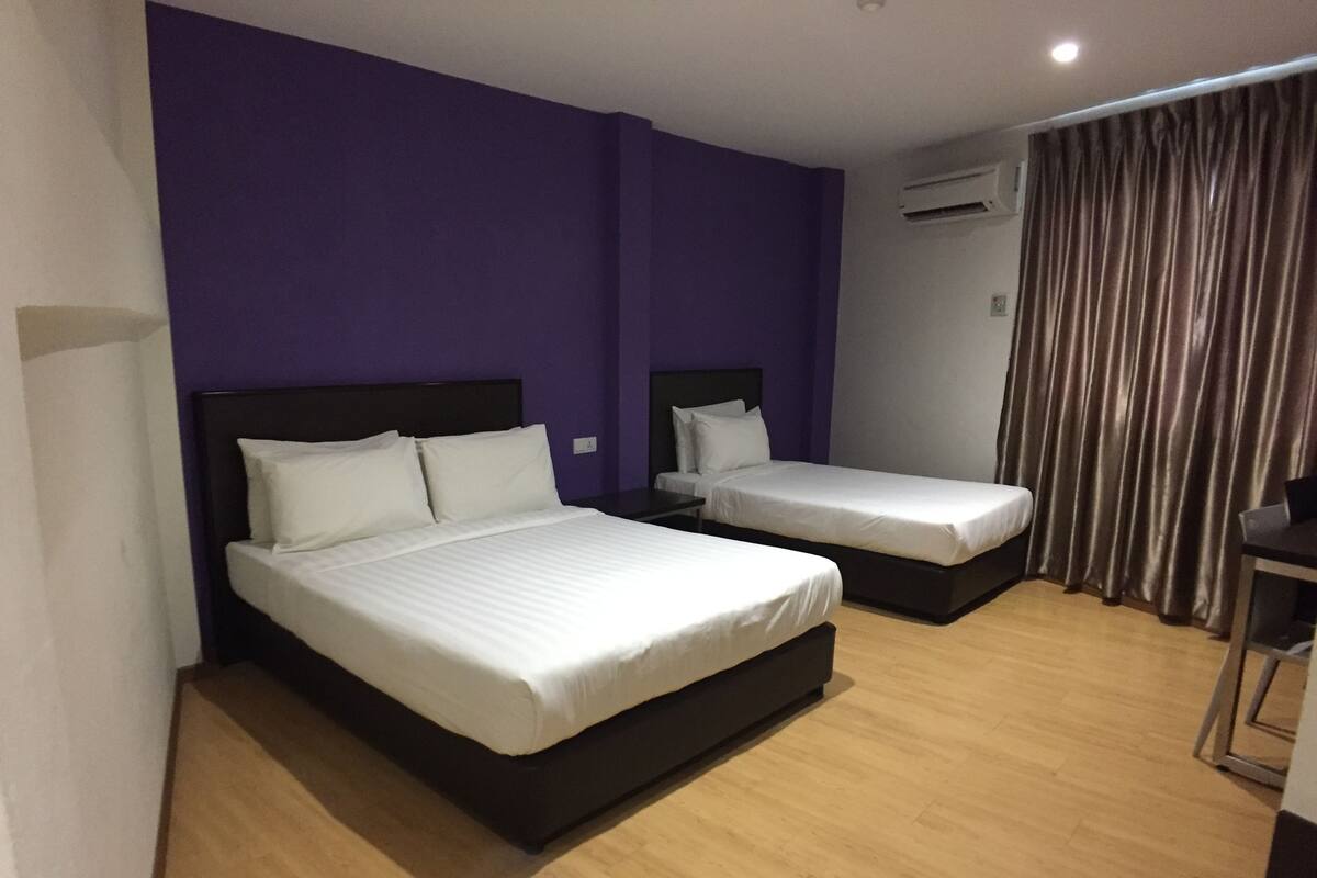 A hotel room with two beds, purple walls, wooden flooring, and a curtain.