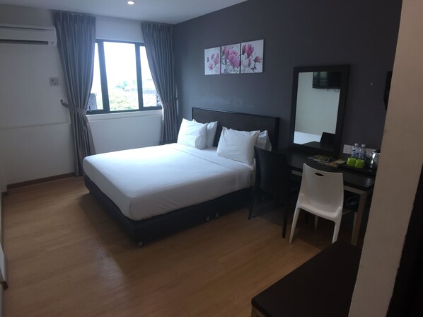 Quarto de hotel com cama, escrivaninha, cadeira, janela com cortinas e espelho fixado na parede.