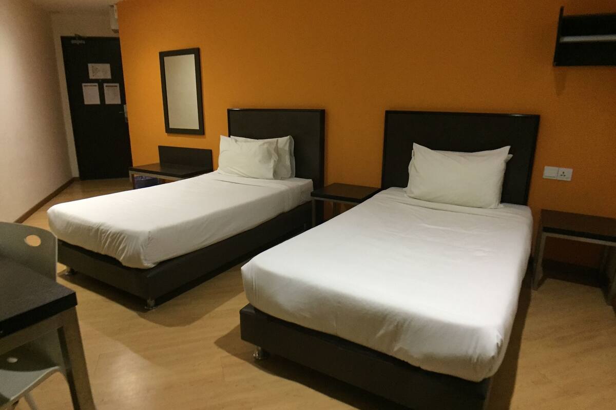 Two single beds with white linens in a room with wooden flooring and orange walls.