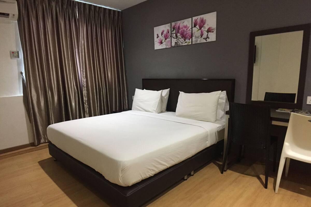 A hotel room with a bed, a desk, a chair, a large mirror, and a painting on the wall.