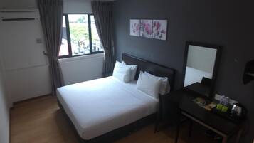 A hotel room with a bed, a desk with a mirror, and a window with curtains.