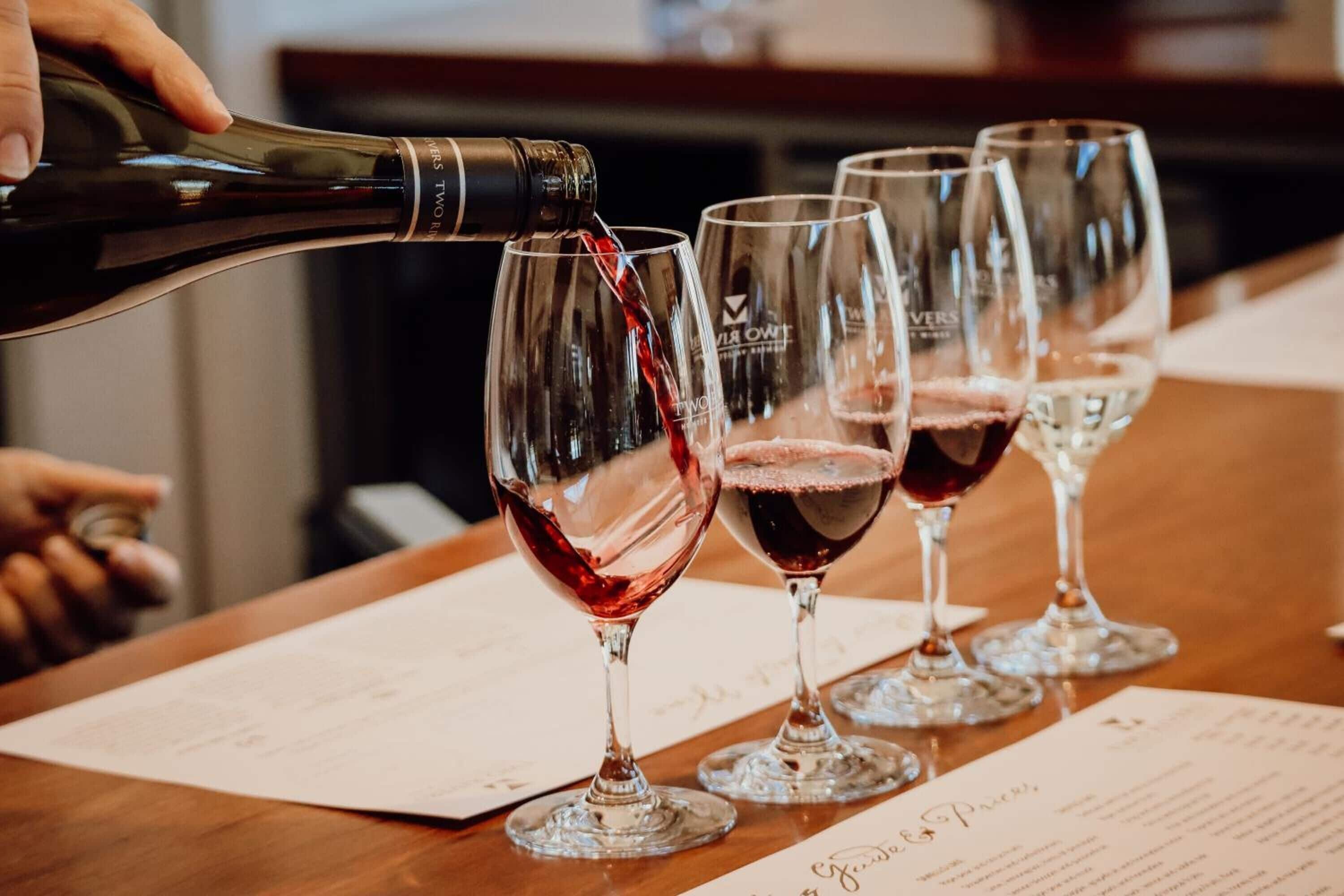 Une personne verse du vin dans des verres à vin sur une table où se trouvent des menus.