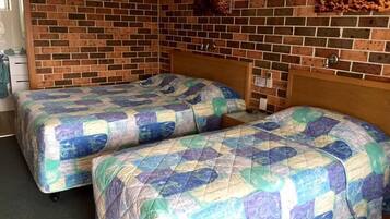 A room with two beds, each with a quilted bedspread, a brick wall, and a picture of food on the wall.