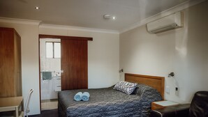 A bedroom with a bed, a desk, a chair, a sofa, and an air conditioning unit. - Denman Motor Inn (Denman)