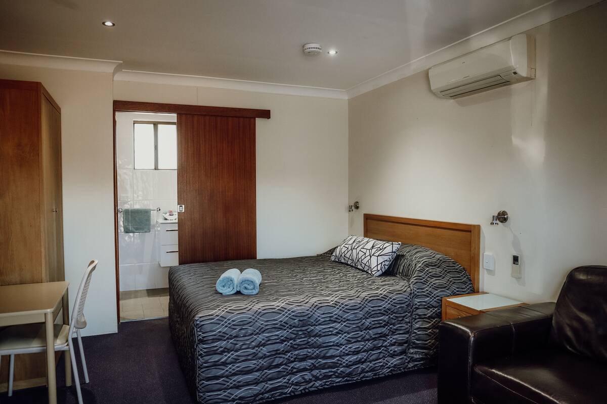 Un dormitorio con cama, escritorio, silla, sofá y aire acondicionado.