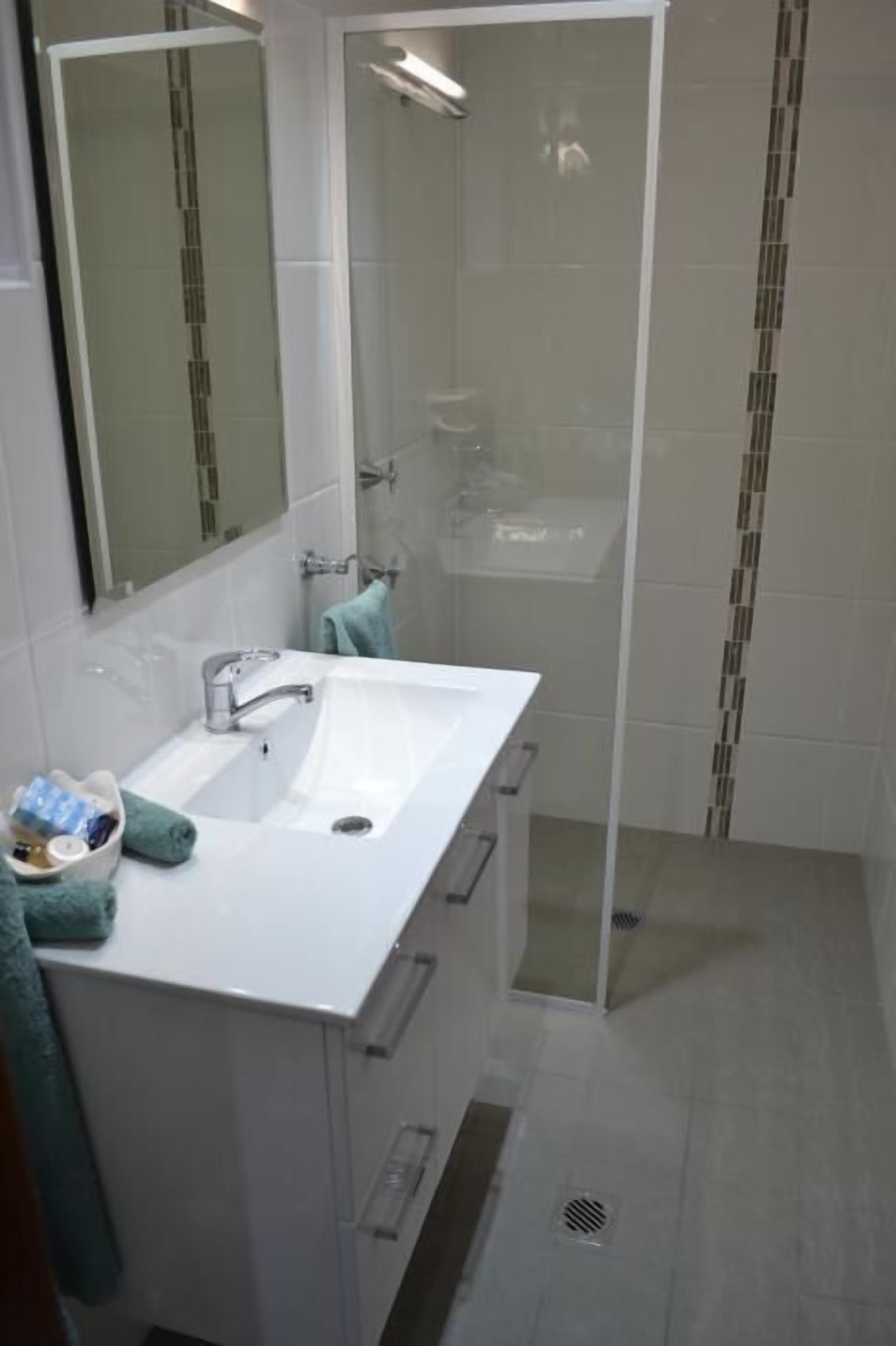 Un baño con lavamanos blanco, espejo y cabina de ducha con paredes de vidrio.