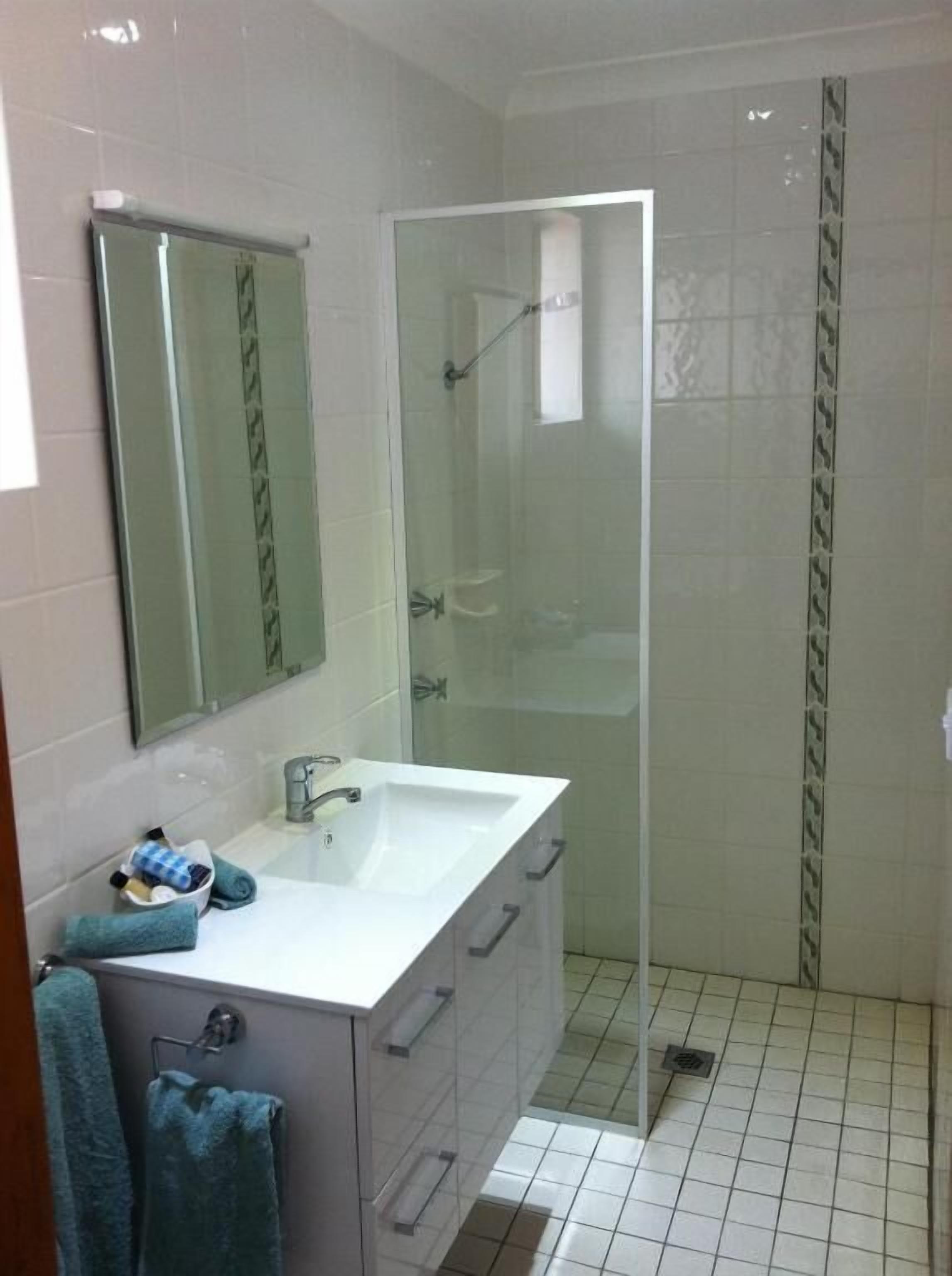 A bathroom with a white sink, a mirror, a glass shower enclosure, and a tiled floor.