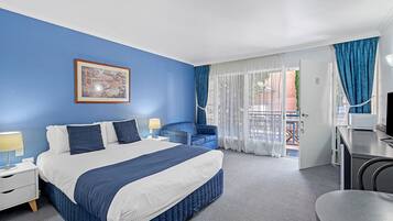 A hotel room with a large bed, a desk, a chair, a nightstand, a lamp, and a view of the outside balcony.