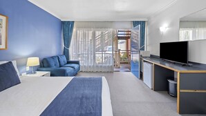 A hotel room with a bed, a desk with a TV, a sofa, and a view of the outside. - The River Boat Hotel - Echuca (Echuca)