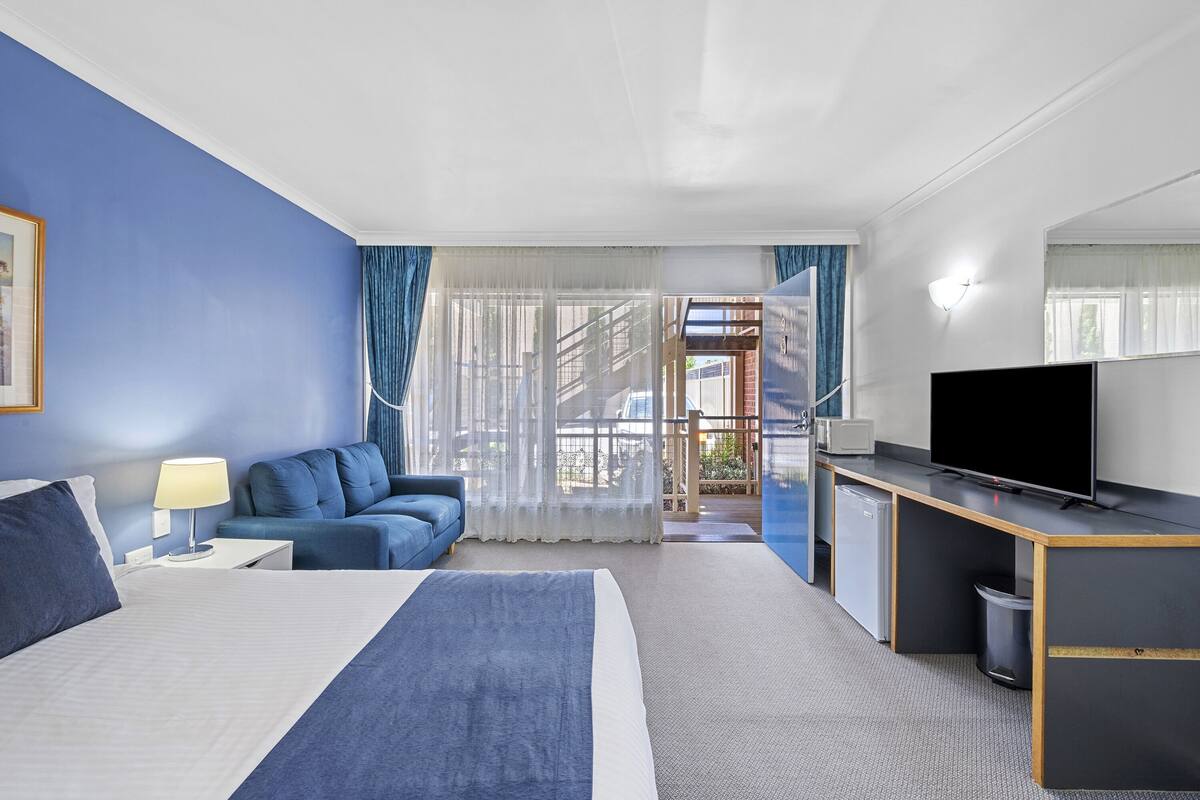 A hotel room with a bed, a desk with a TV, a sofa, and a view of the outside.