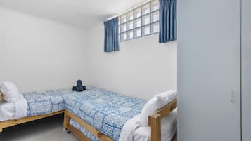 A small, single-bed room with a wooden frame, a patterned blue and white bedspread, and a window with blue curtains.