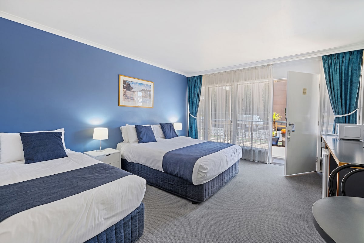 A hotel room with two beds, a desk, and a view of the city.