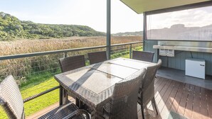 Un espace extérieur abrité, équipé d’une table et de chaises, d’un réfrigérateur, et offrant une vue sur un champ et des collines.