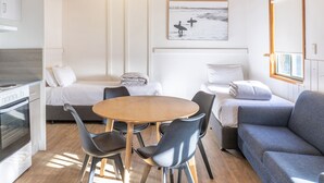Une pièce moderne et bien éclairée, avec un plafond en bois, une table à manger entourée de chaises, un canapé et un lit recouvert de linge de lit blanc.