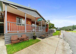 A building with a porch, a sign reading "OFFICE", and a grassy area with benches. - NRMA Port Campbell Holiday Park (Port Campbell)