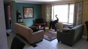 A living room with a sofa, a small table, a television, and a window with curtains. - Tanoshii Spa & The Edge Spa Stay (Goonellabah)