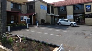 A parking lot with a white car parked in front of a building with multiple businesses, including a coffee shop and a store named 'EDGE'. - Tanoshii Spa & The Edge Spa Stay (Goonellabah)