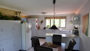A compact kitchen with a dining area, white cabinets, a refrigerator, and a hanging light fixture. - Tanoshii Spa & The Edge Spa Stay (Goonellabah)