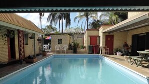 A swimming pool with a tiled deck, surrounded by buildings with brick walls and red doors. - Tanoshii Spa & The Edge Spa Stay (Goonellabah)