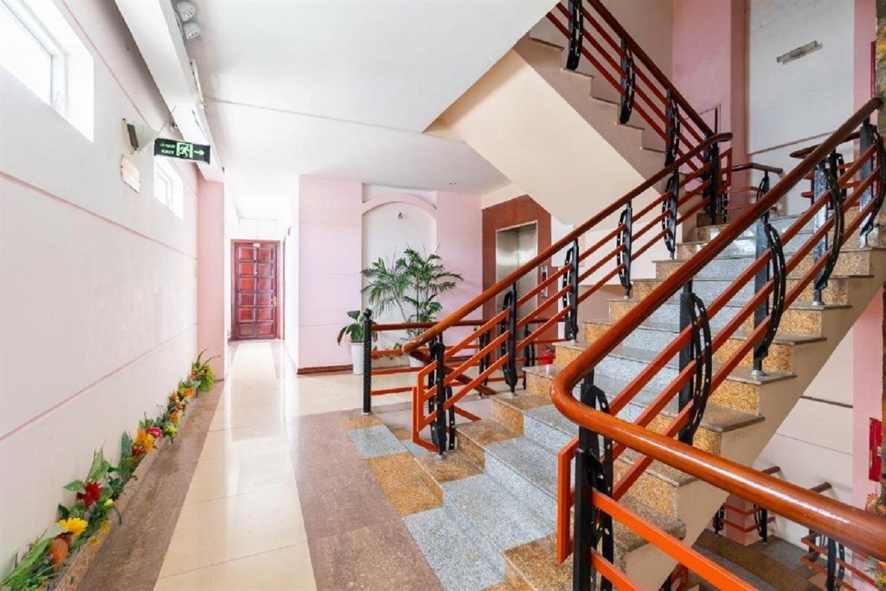 Un vestíbulo de hotel con una escalera, un mostrador de recepción y una planta.