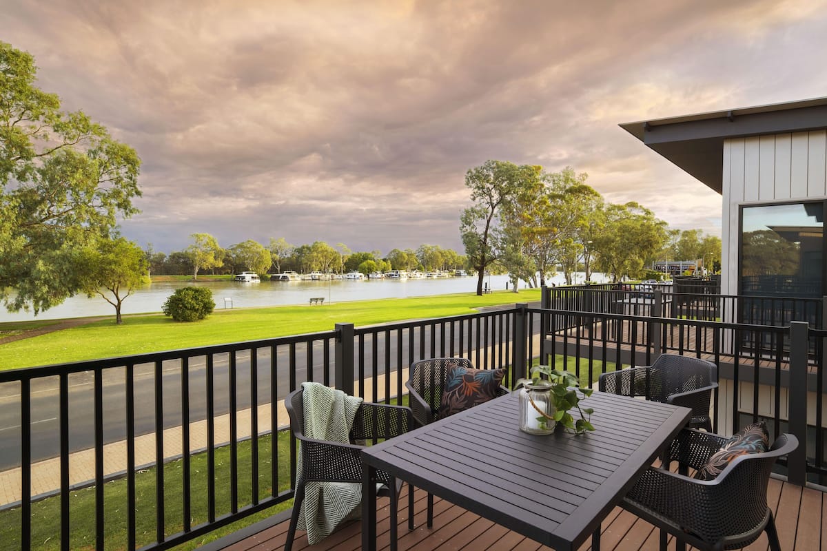 A deck with outdoor seating, a view of a lake, and a building with large windows.