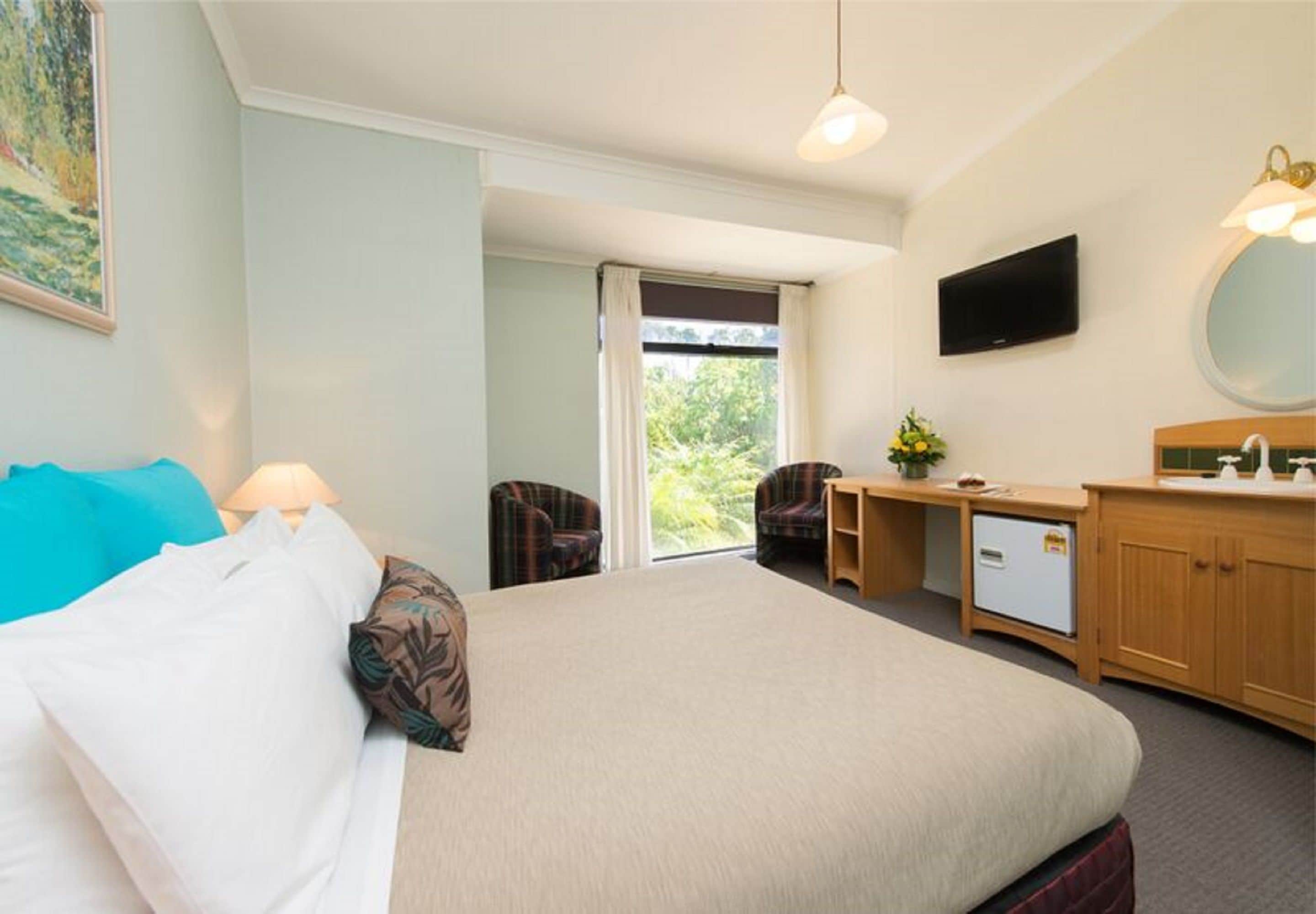 A hotel room with a bed, a desk, a chair, a television, and a bathroom with a mirror and sink.