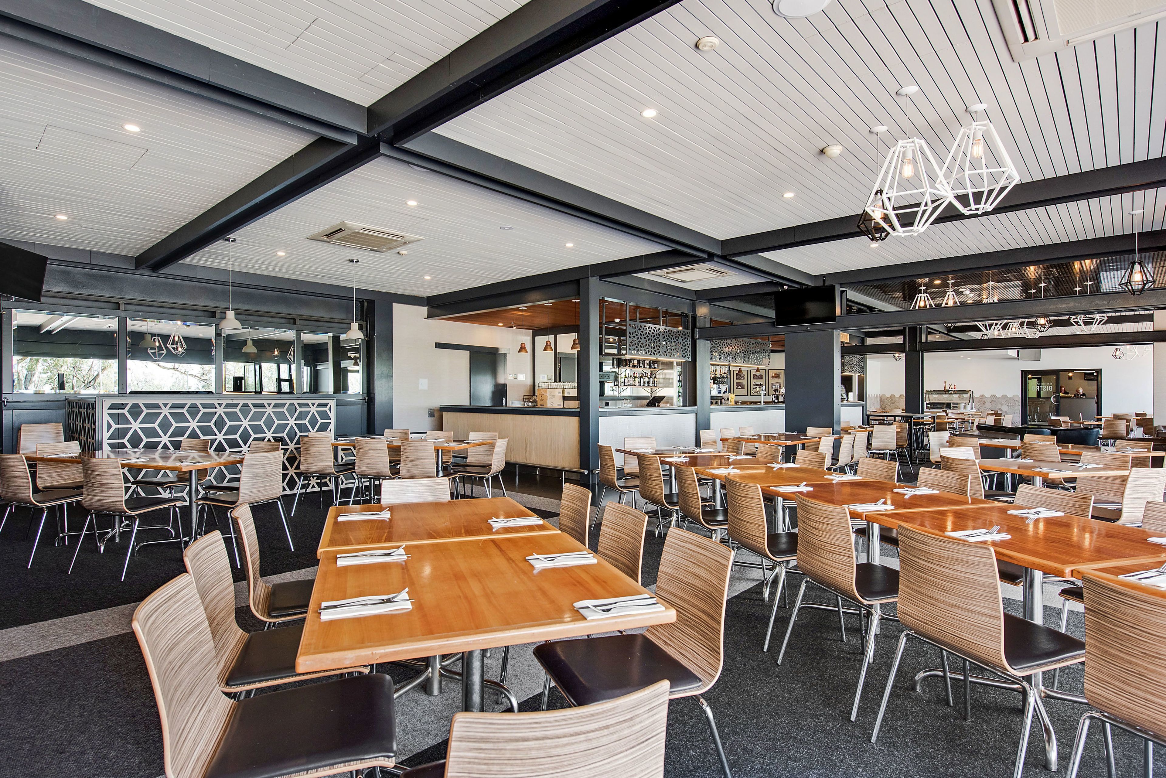 A spacious dining area with multiple tables and chairs, a modern ceiling design, and a visible kitchen area in the background.