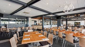 A spacious dining area with multiple tables and chairs, a modern ceiling design, and a visible kitchen area in the background.