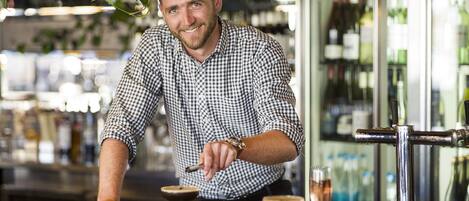Un cantinero en un bar, con camisa a cuadros, un reloj y un cóctel en un vaso.