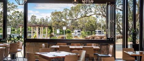 Un restaurante con terraza, amplios ventanales y lámparas colgantes.