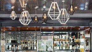 A bar area with hexagonal pendant lights, a counter with various bottles, and a seating area with a table. - Berri Hotel (Berri)
