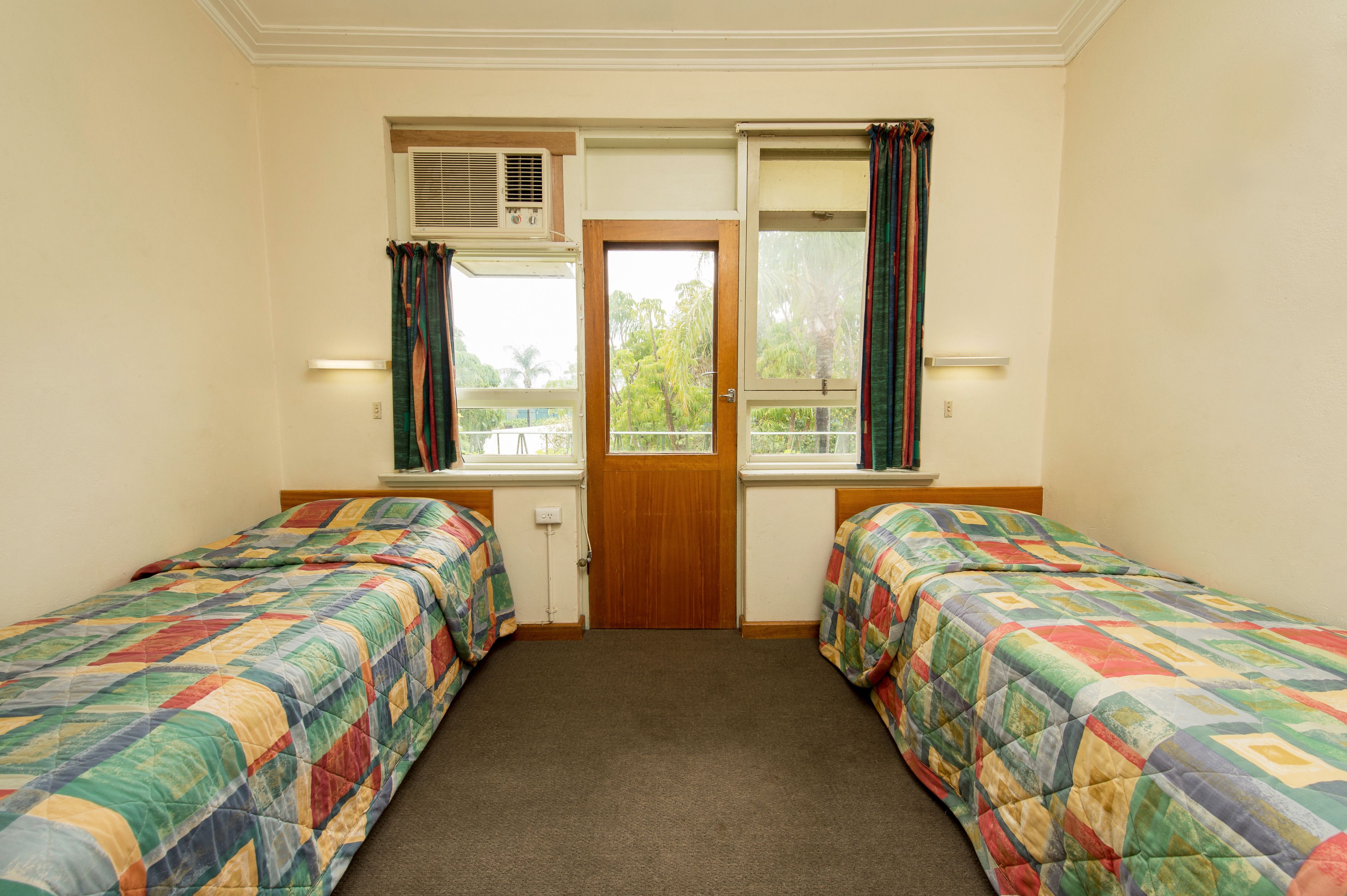 A room with two single beds, a wooden door, and windows with curtains.