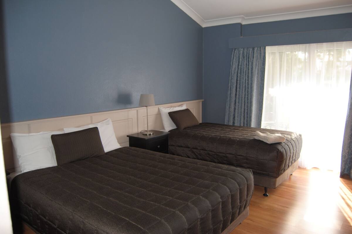 A hotel room with two beds, a nightstand, and a window with curtains.
