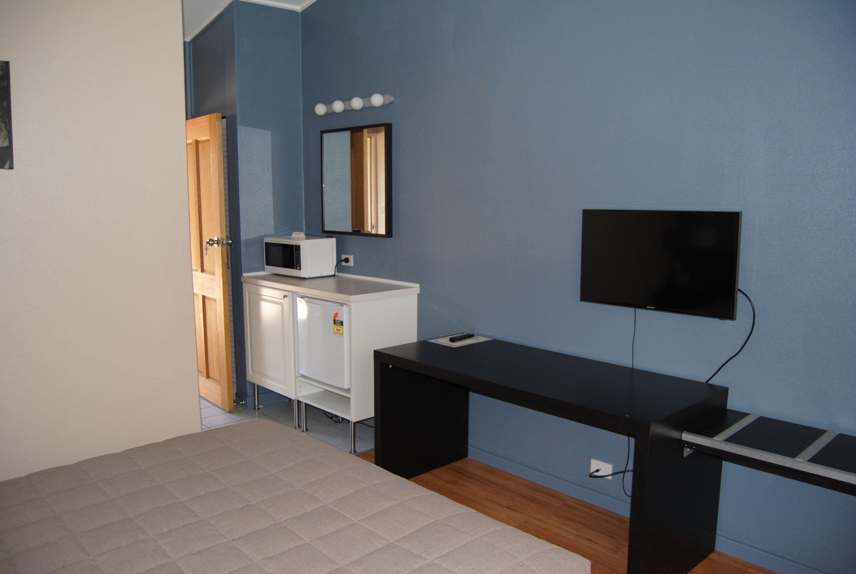 Ein Zimmer mit einem Bett, einem Schreibtisch, einer Mikrowelle, einem Spiegel und einem Fernseher.