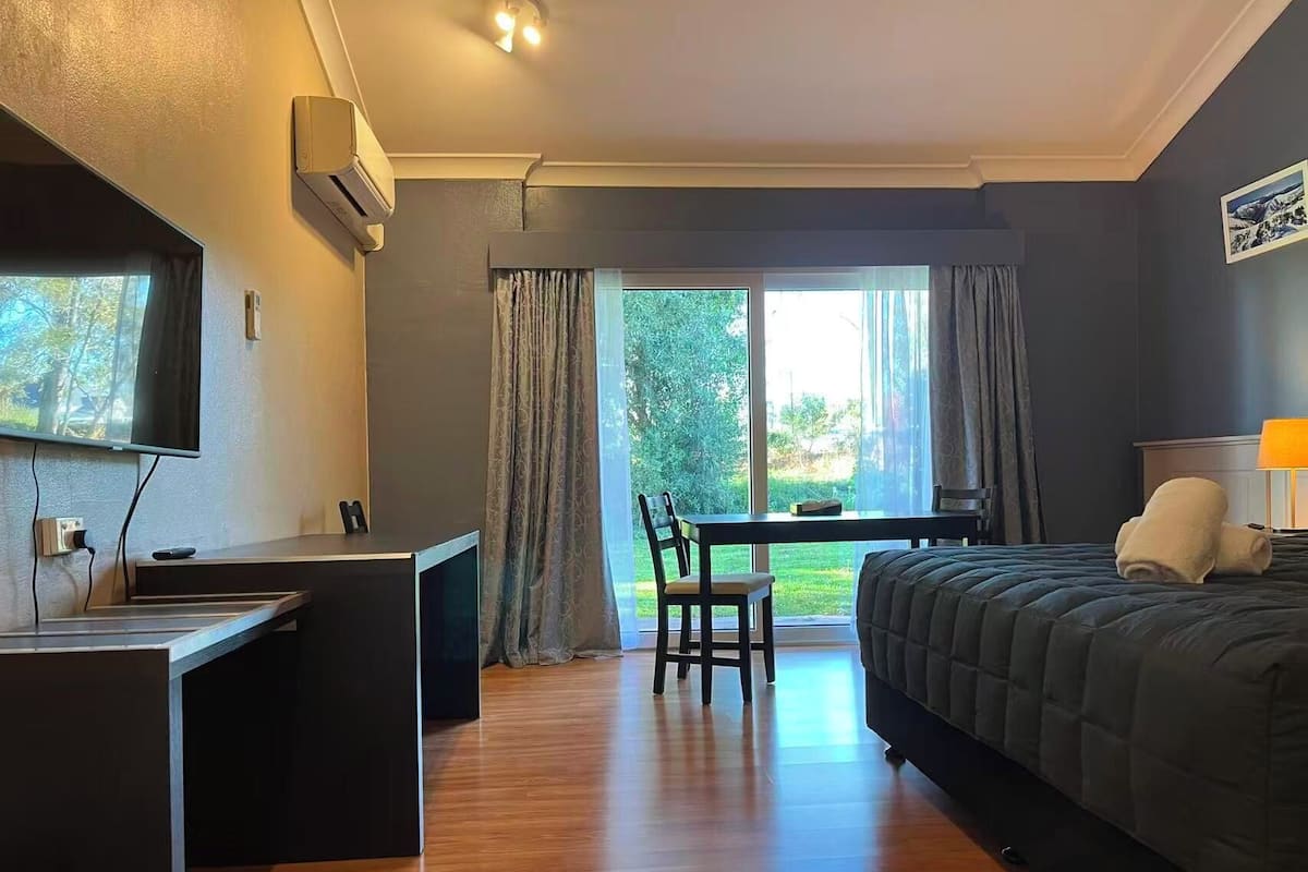 A compact hotel room with a bed, a desk, and a chair. There is a window providing a view of the outdoors.