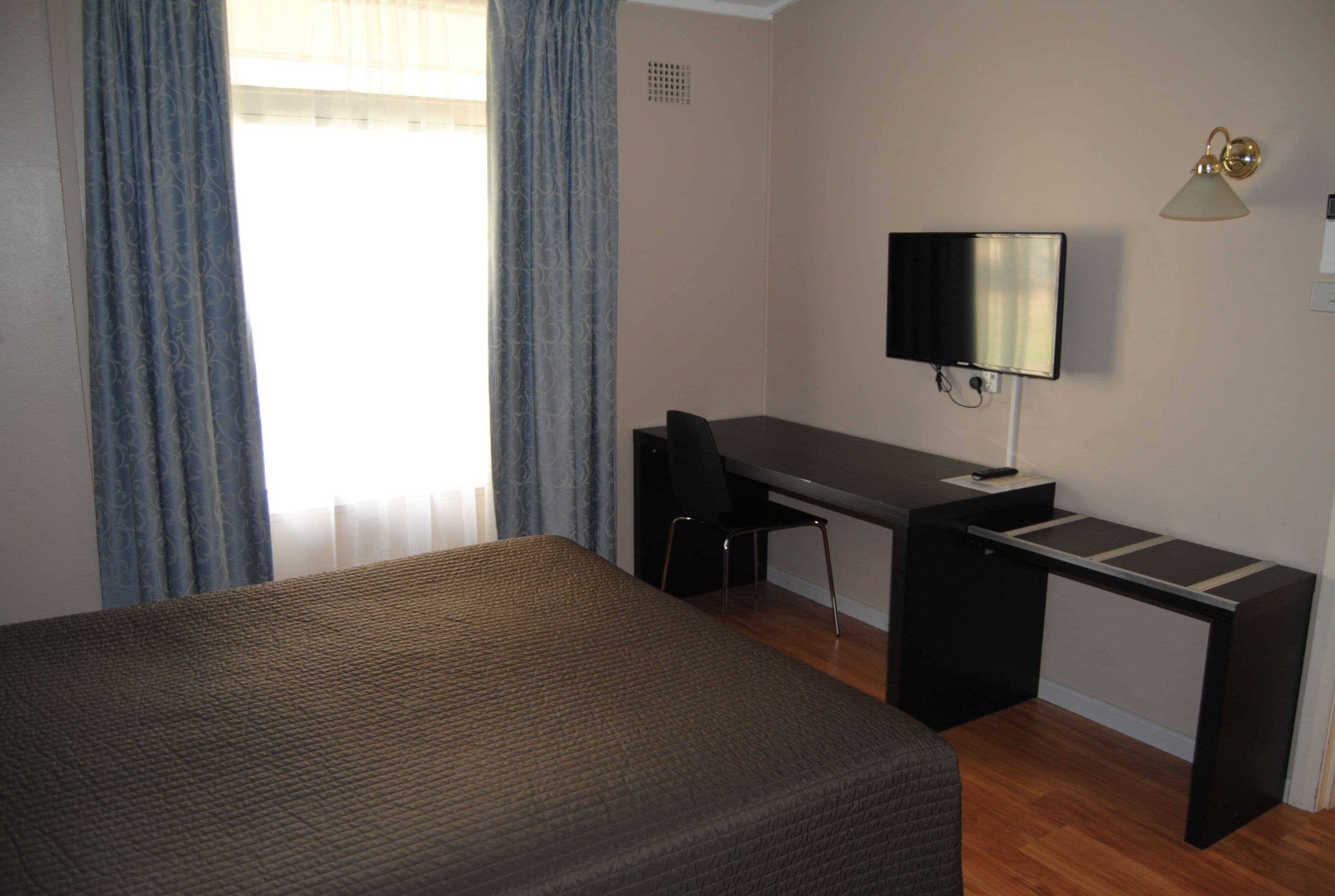 A hotel room with a bed, a desk, a chair, a television, and a lamp.