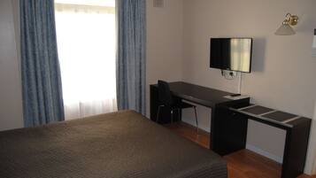 A hotel room with a bed, a desk, a chair, a television, and a lamp.