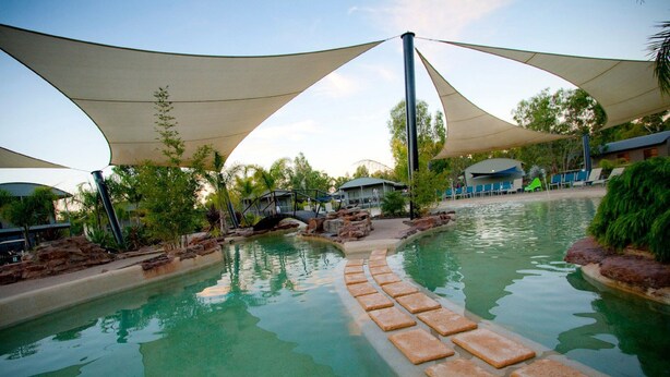 A swimming pool with stepping stones leading into the water, surrounded by shaded areas and greenery.
